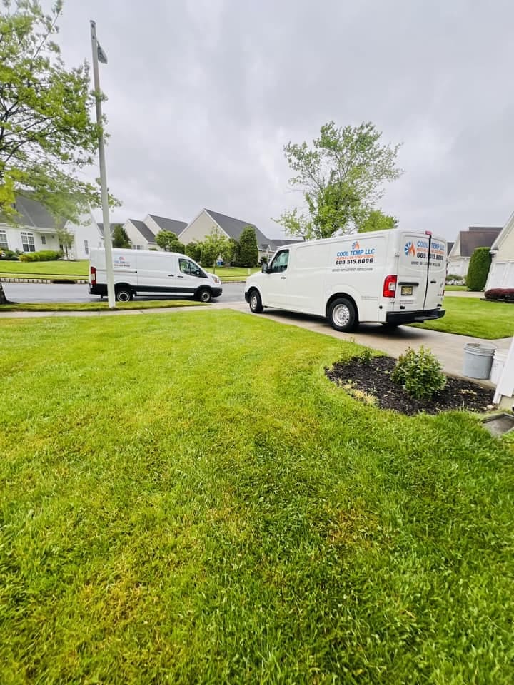 Two white service vans parked on a residential street, with trees and houses in the background on a cloudy day.