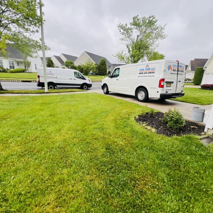 Two white service vans parked on a residential street, with trees and houses in the background on a cloudy day.