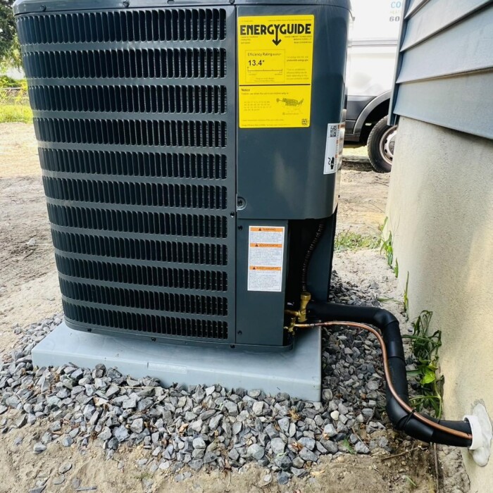An outdoor air conditioning unit on a concrete pad with an EnergyGuide label, surrounded by gravel and a nearby building wall.